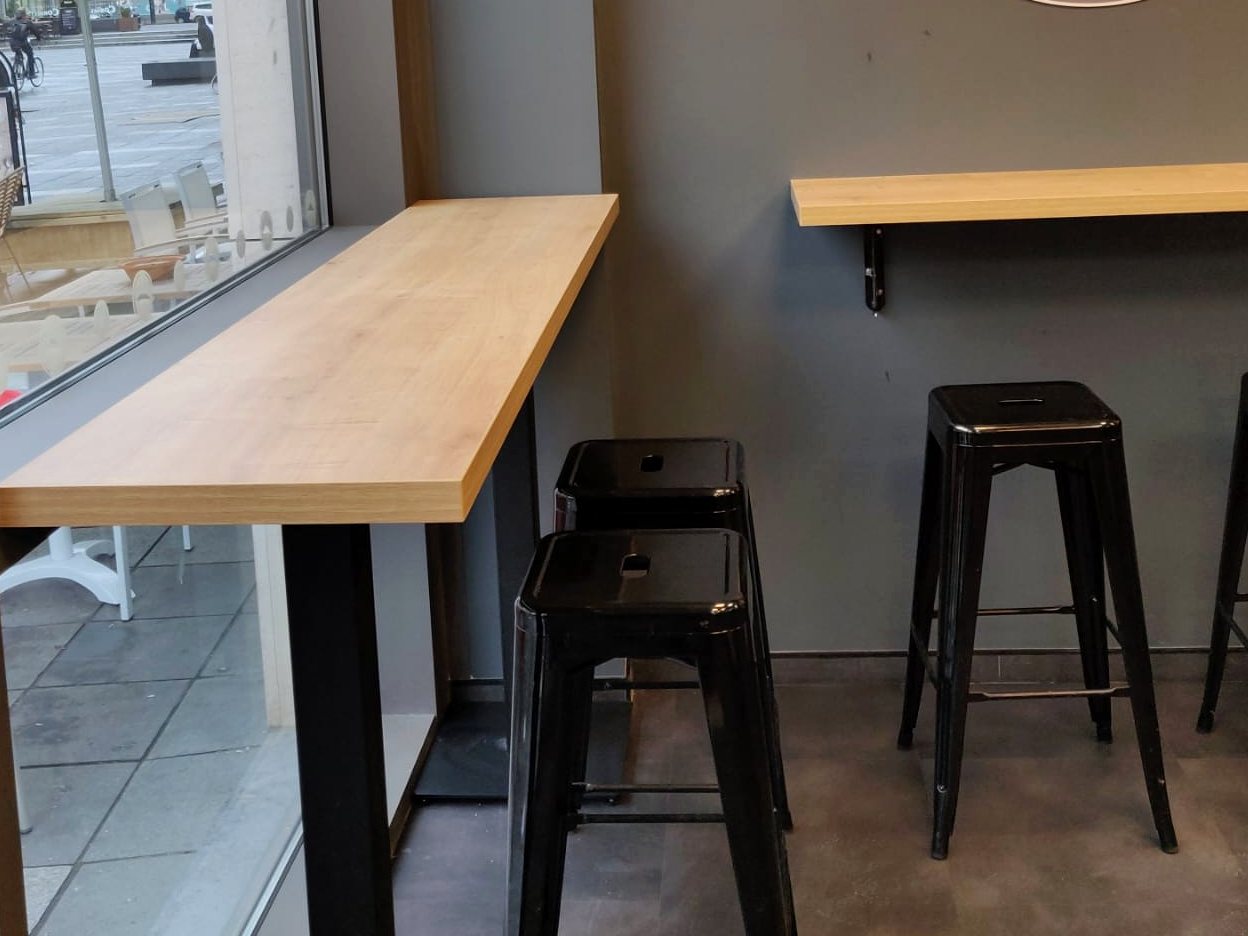 Houten bartafels langs het raam en de wand met zwarte barkrukken
