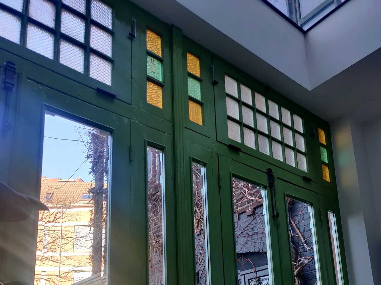Groene openslaande deuren met gekleurd glas in de bovenlichten, van binnenuit